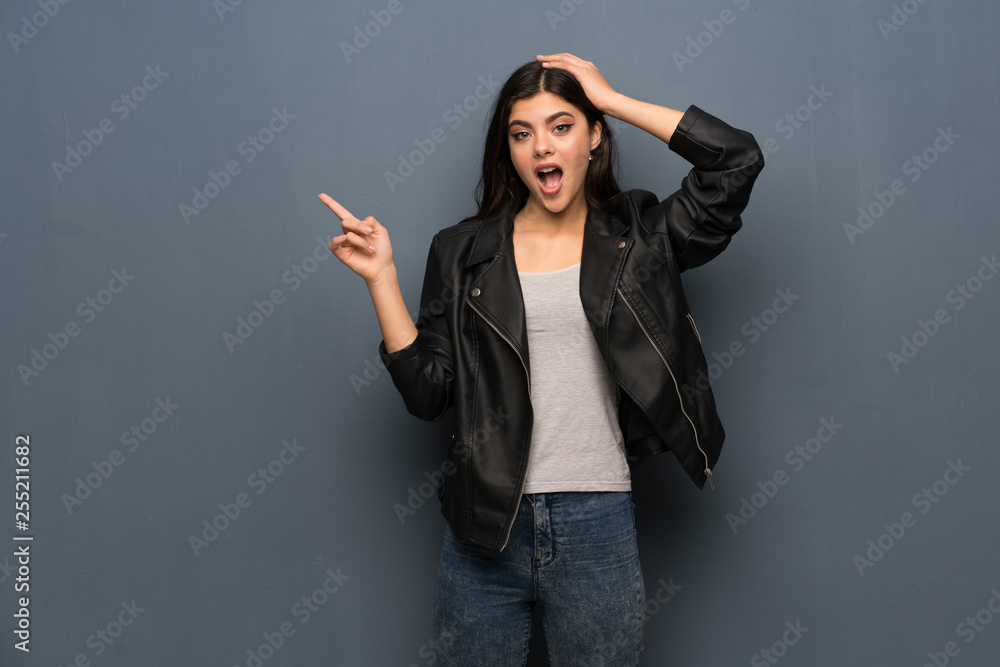 Teenager girl over grey wall surprised and pointing finger to the side Teenager girl over grey wall surprised and pointing finger to the side