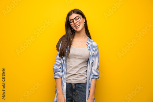 Teenager girl over yellow wall with glasses and happy