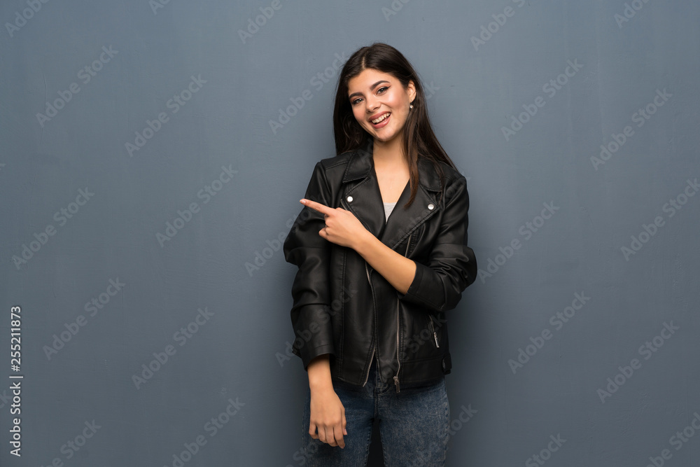 Teenager girl over grey wall pointing to the side to present a product Teenager girl over grey wall pointing to the side to present a product