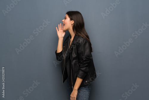 Teenager girl over grey wall shouting with mouth wide open to the lateral © luismolinero