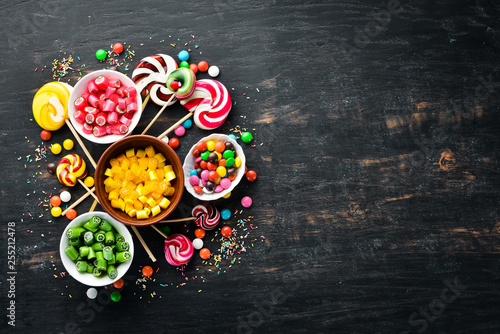 Background of colored candies and lollipops. Sweets. On a black background. Top view. free copying space.