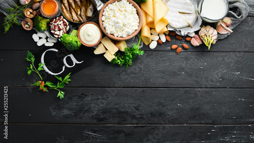 Products containing natural calcium: cheese, milk, parmesan, sour cream, fish, almonds, parsley, garlic, broccoli. On a black wooden background. Top view. Free copy space.