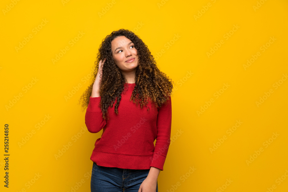 Teenager girl with red sweater over yellow wall thinking an idea while scratching head Teenager girl with red sweater over yellow wall thinking an idea while scratching head