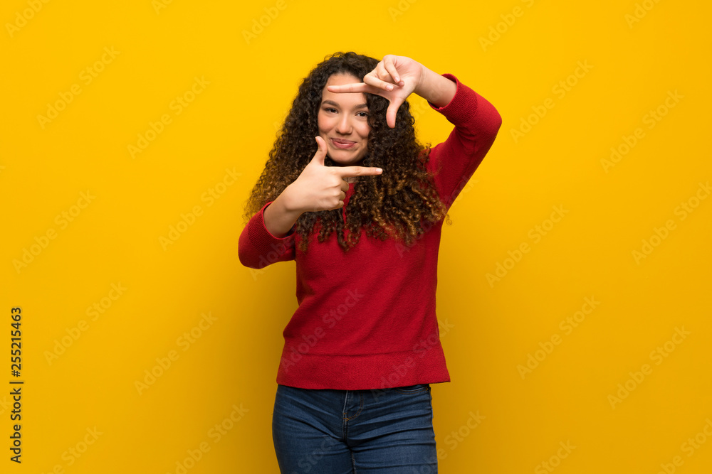 Teenager girl with red sweater over yellow wall focusing face. Framing symbol Teenager girl with red sweater over yellow wall focusing face. Framing symbol