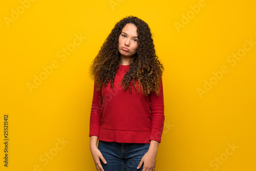 Teenager girl with red sweater over yellow wall with sad and depressed expression