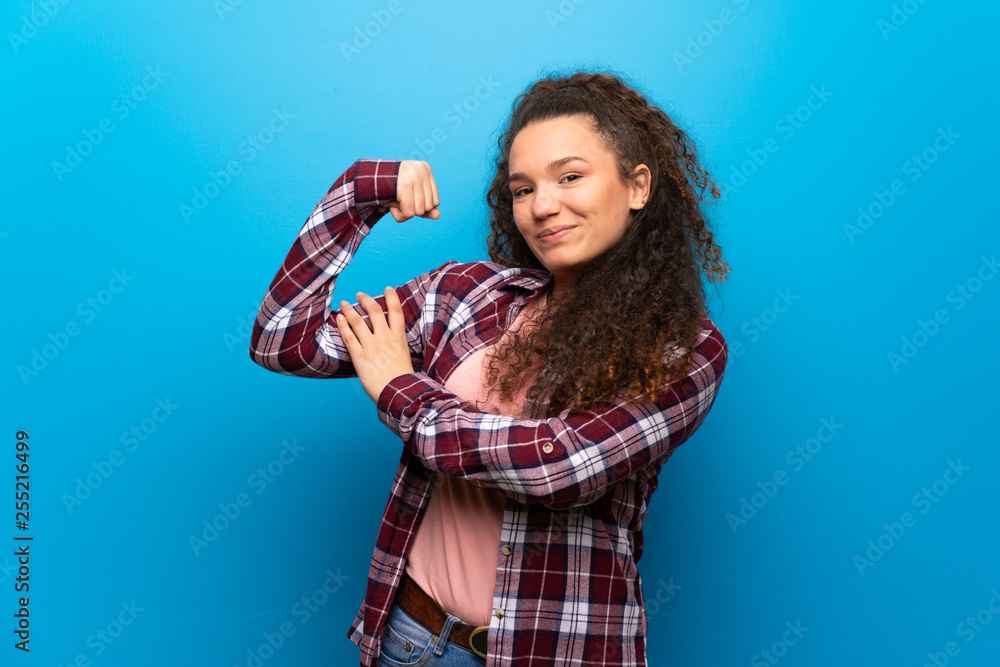 Teenager girl over blue wall proud and self-satisfied