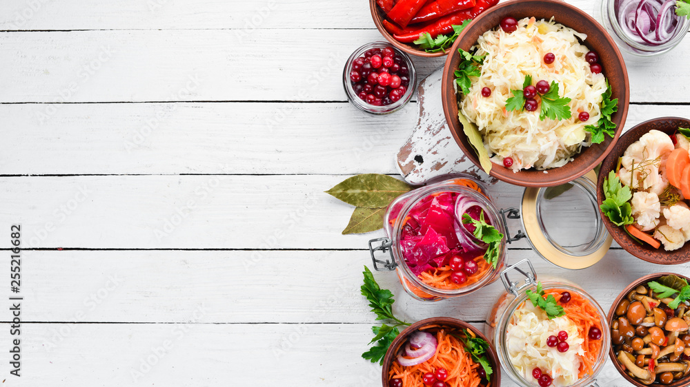 Pickled vegetables and mushrooms in a white kitchen table. Cabbage, mushrooms, cucumbers, cauliflower. Top view. Free space for your text. Pickled vegetables and mushrooms in a white kitchen table. Cabbage, mushrooms, cucumbers, cauliflower. Top view. Free space for your text.