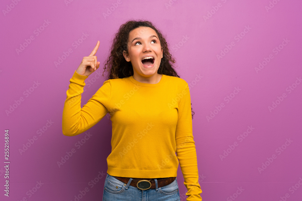 Teenager girl over purple wall intending to realizes the solution while lifting a finger up Teenager girl over purple wall intending to realizes the solution while lifting a finger up