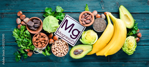 Foods containing natural magnesium. Mg: Chocolate, banana, cocoa, nuts, avocados, broccoli, almonds. Top view. On a blue wooden background. photo