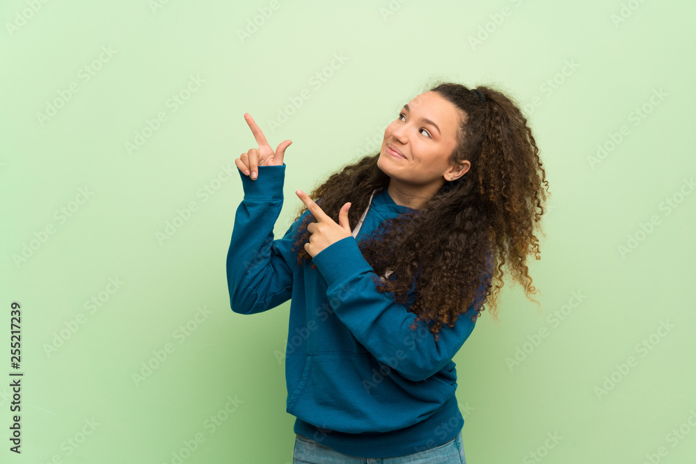 Teenager girl over green wall pointing with the index finger and looking up Teenager girl over green wall pointing with the index finger and looking up