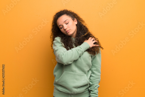 Teenager girl over ocher wall suffering from pain in shoulder for having made an effort © luismolinero