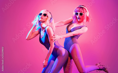 Fashion. Two sexy DJ girl in Colorful neon light having fun dance, friends. Glamour party fitness woman with Dyed Hair. Young beautiful fashionable model enjoy dancing. Funny art neon style