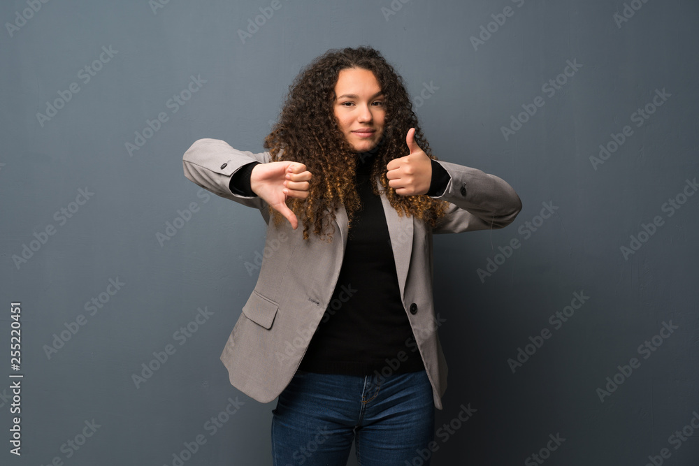 Teenager girl over blue wall making good-bad sign. Undecided between yes or not