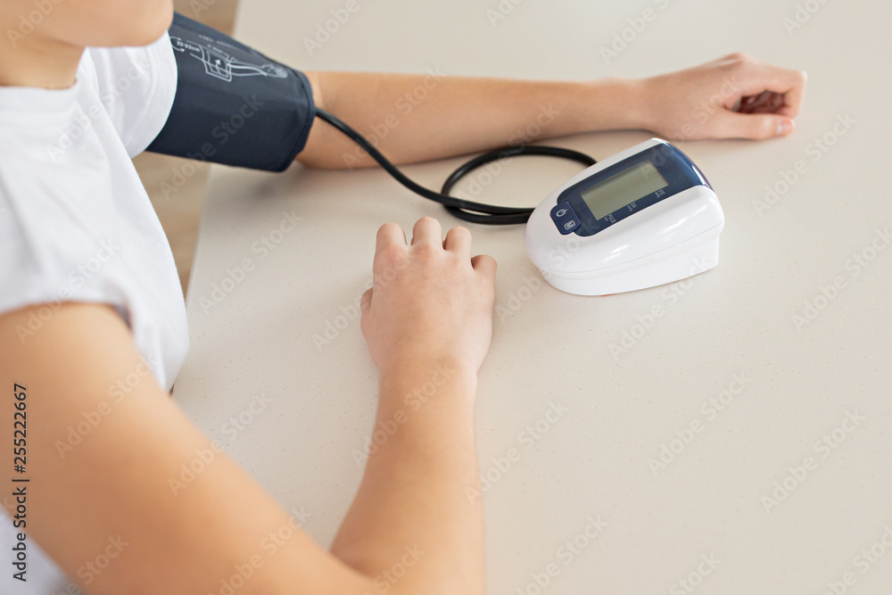 Hypertension concept. Teenager is measuring blood pressure with monitor in home. Hands close-up