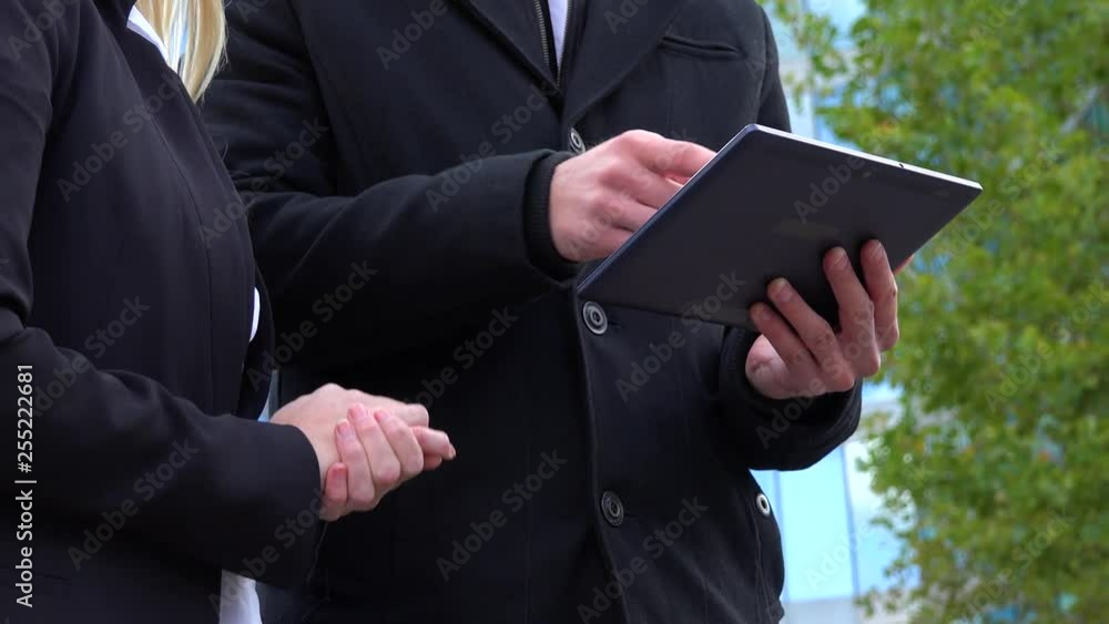 A businessman and a businesswoman work on a tablet in front of an office building - closeup A businessman and a businesswoman work on a tablet in front of an office building - closeup