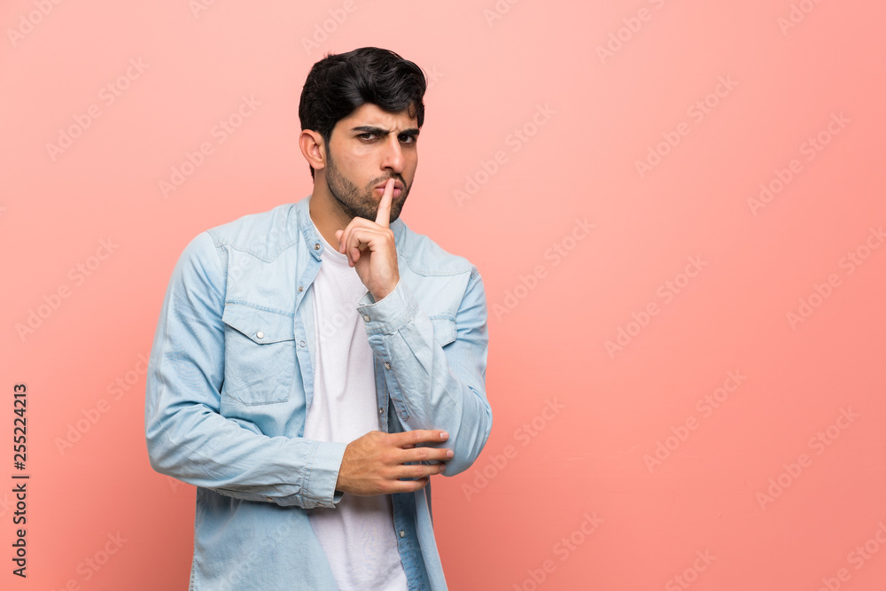 Young man over pink wall showing a sign of silence gesture putting finger in mouth Young man over pink wall showing a sign of silence gesture putting finger in mouth