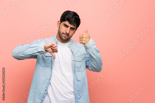 Young man over pink wall making good-bad sign. Undecided between yes or not