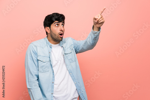 Young man over pink wall pointing away