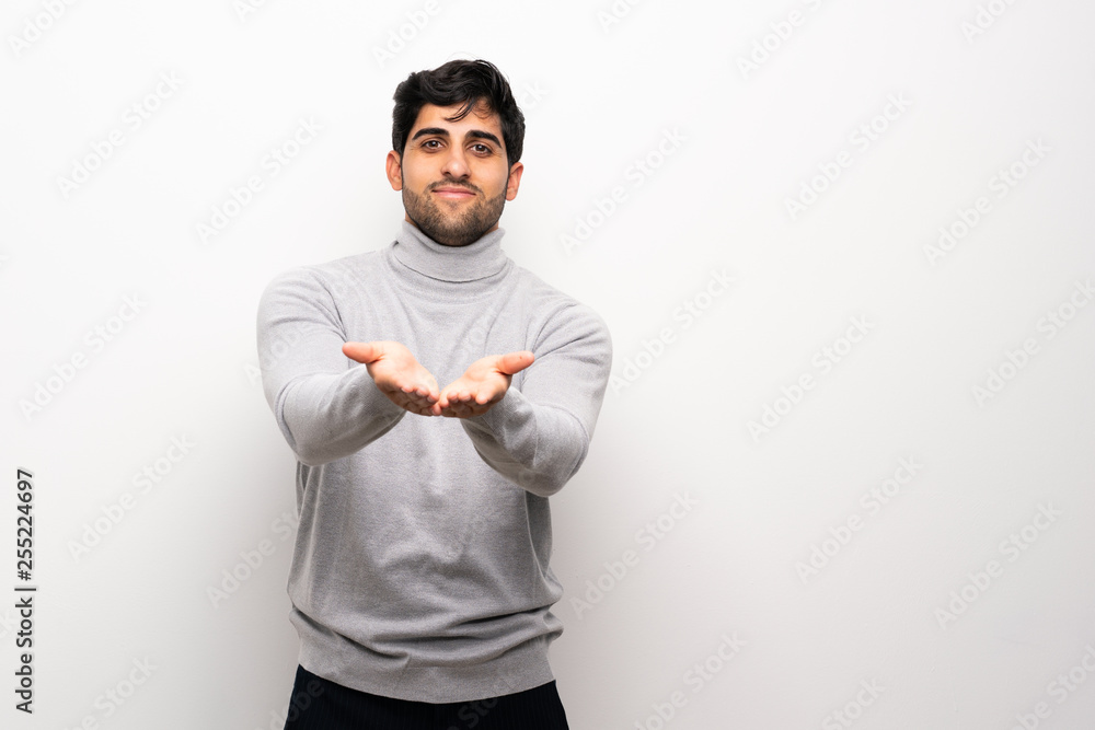 Young man over isolated white wall holding copyspace imaginary on the palm to insert an ad Young man over isolated white wall holding copyspace imaginary on the palm to insert an ad