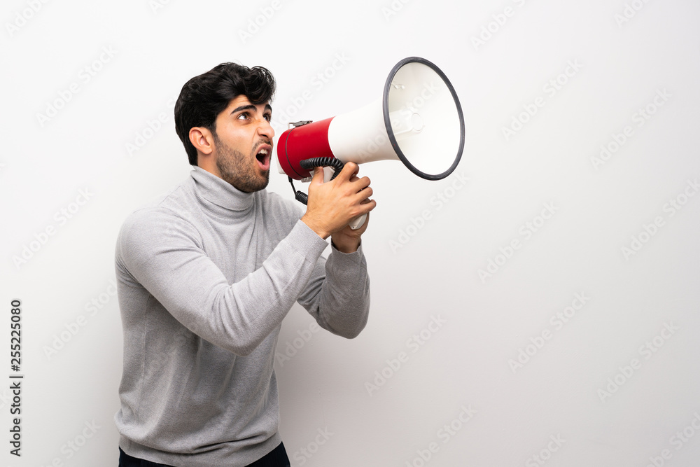 Young man over isolated white wall shouting through a megaphone Young man over isolated white wall shouting through a megaphone