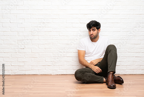 Young man sitting on the floor with sad and depressed expression © luismolinero