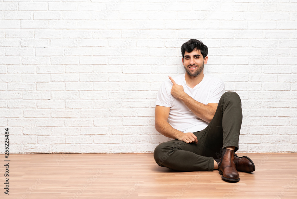 Young man sitting on the floor pointing to the side to present a product Young man sitting on the floor pointing to the side to present a product