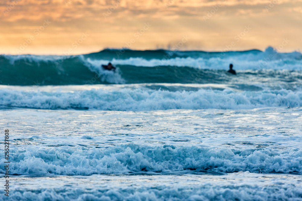 Fototapeta premium Sufers riding into colorful sunset at Piha Beach, New Zealand