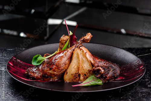 Exclusive restaurant meals. Duck confit with baked pear and cranberry sauce served on snow dark plate on black table background. copy space