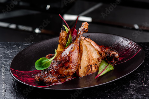 Exclusive restaurant meals. Duck confit with baked pear and cranberry sauce served on snow dark plate on black table background. copy space photo