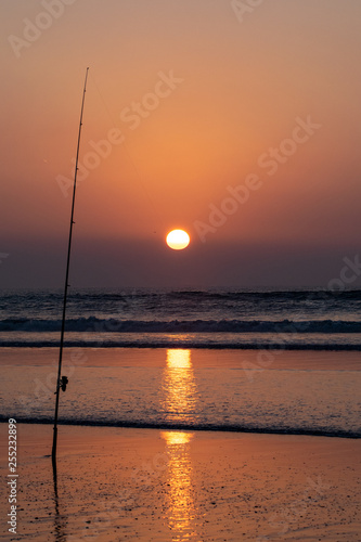 Silhouette of fishing rod at the edge of the Atlantic Ocean at sunset from Agadir beach, Morocco, Africa