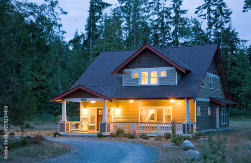 Traditional Craftsman style home exterior with outdoor lighting lights on and light shining through windows at dusk night