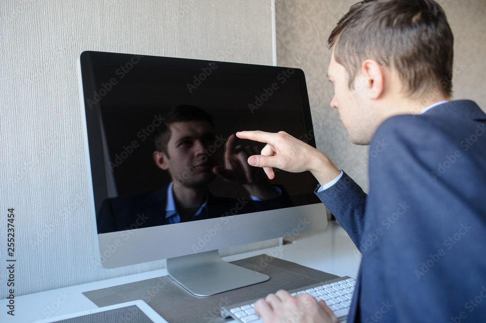 Obraz premium lateral view of a young man sitting in front of a computer and showing something with his finger on monitor
