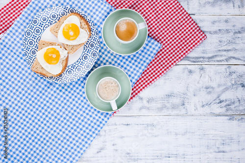 Toast with a heart-shaped egg on a plate and 2 cups of coffee. Romantic breakfast for two. White wooden background and napkin with food. Free space for text. photo