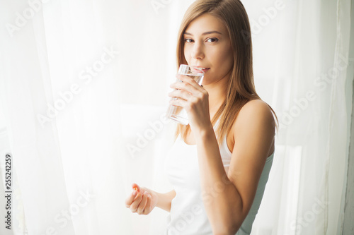 Health concept. Young woman holding pill and glass of water