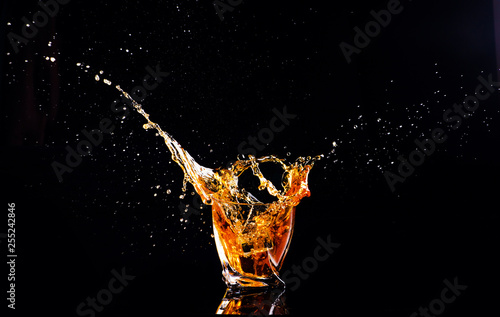 whiskey with splash on black background, brandy in a glass © The Len