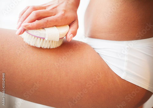 Woman scrubbing her legs with a brush making skin peeling in the bathroom