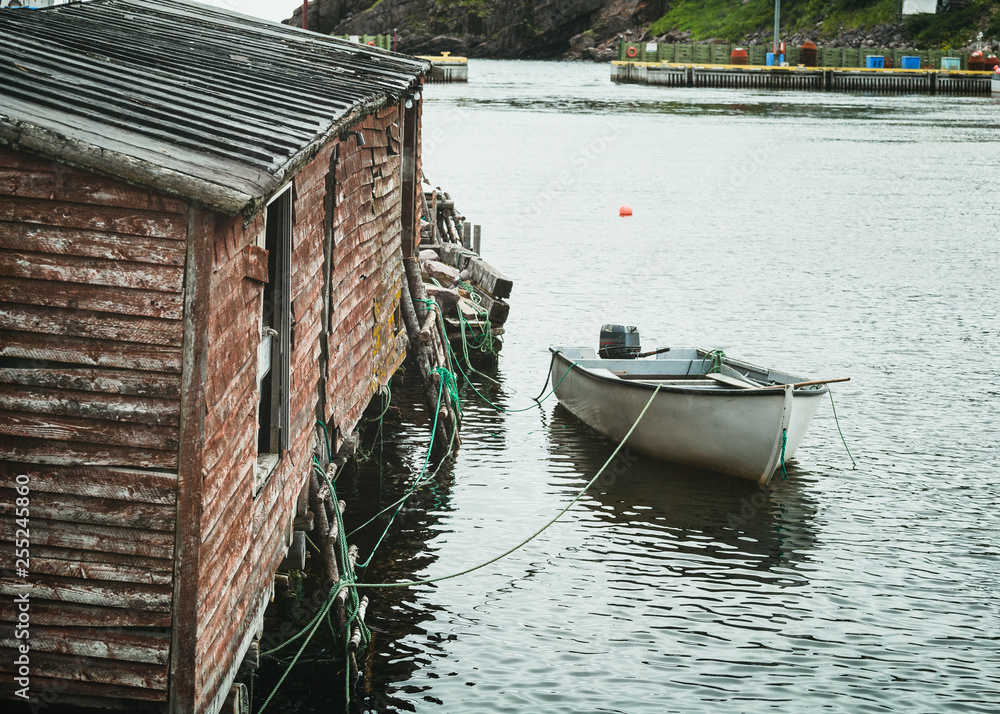 Small fishing boat tied up to a fishing shed in a safe harbor along the coast of Newfoundland, Canada.