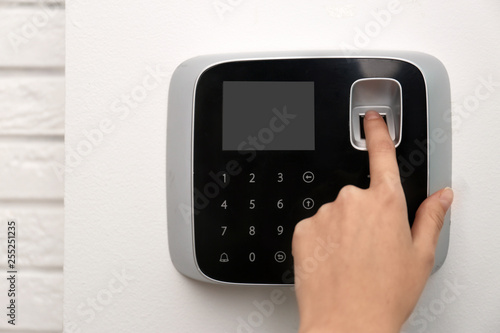 Woman scanning fingerprint on alarm system indoors, closeup