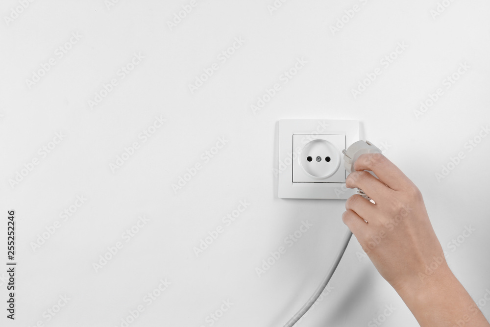 Woman putting plug into power socket on white background, closeup. Electrician's equipment Woman putting plug into power socket on white background, closeup. Electrician's equipment