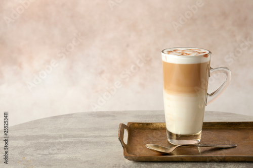 Tray with glass cup of caramel macchiato and syrup on table against color background. Space for text photo