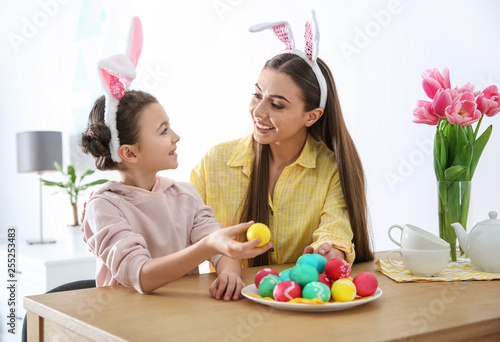 Mother and daughter with bunny ears headbands and painted Easter eggs at home