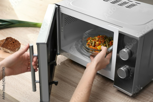 Young woman using microwave oven on table in kitchen photo