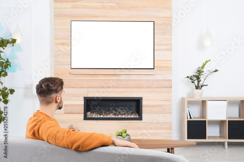 Man watching TV on sofa in living room with decorative fireplace