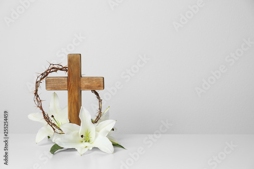 Φωτογραφία Wooden cross, crown of thorns and blossom lilies on table against light backgrou