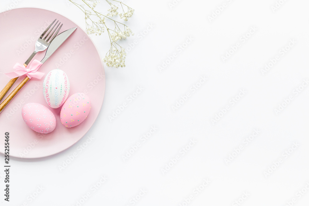 Easter dining table in pastel colors. Plate, cutlery, painted eggs, gingerbread and dry flower branch on white background top view space for text Easter dining table in pastel colors. Plate, cutlery, painted eggs, gingerbread and dry flower branch on white background top view space for text