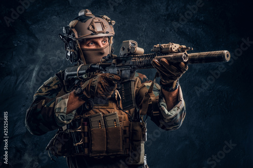 Obraz na płótnie Elite unit, special forces soldier in camouflage uniform holding an assault rifle with a laser sight and aims at the target