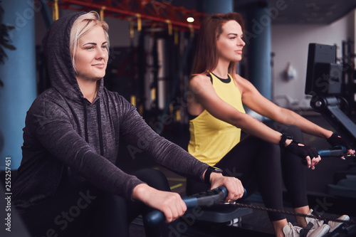 Two beautiful young women doing rowing practice in the modern gym