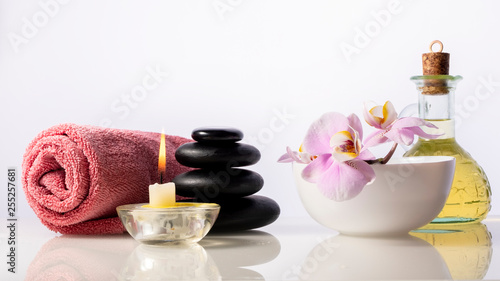 Zen spa stones, orchid flower in bowl, candle, bottle with oil and towel. Spa composition isolated on white background.