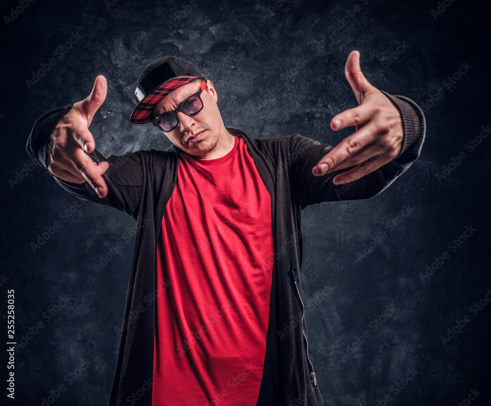 Portrait of a young rapper dressed in a hip-hop style, posing for a camera. Studio photo against a dark textured wall Portrait of a young rapper dressed in a hip-hop style, posing for a camera. Studio photo against a dark textured wall