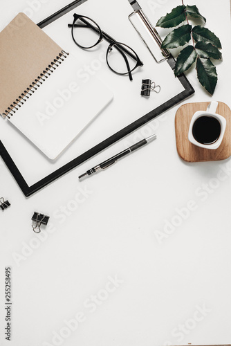 Home office workspace mockup with blank clip board  office supplies  pen  green leaf  coffee cup and eyeglasses on white background. Flat lay  top view  copy space